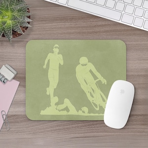 May include: A light green mousepad featuring a triathlon design. The design includes illustrations of a runner, a cyclist, and a swimmer. A white computer mouse is on the right side of the mousepad. The mousepad is on a wooden desk.