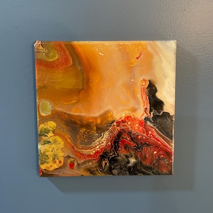 May include: Square abstract painting with a fluid design. The artwork features a blend of warm colors, including orange, red, yellow, and black, creating a dynamic and textured visual effect. The piece is mounted on a square canvas.