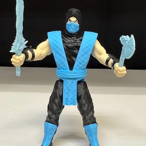 May include: A plastic action figure of a ninja character wearing a black hood, mask, and suit with a light blue quilted vest, belt, and shin guards. The figure holds a light blue translucent sword in the right hand and a light blue axe in the left.