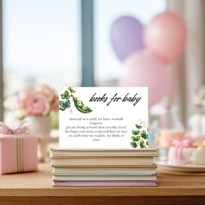 May include: A white card with the text "books for baby" and a request for guests to bring a book. The card features a watercolor illustration of peas in a pod and green vines. The card is placed on a stack of books.