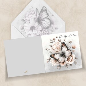 May include: A greeting card with a watercolor butterfly and floral design. The card features a butterfly with brown and white wings, surrounded by light pink and white flowers. The text "One day at a time" is written on the card.