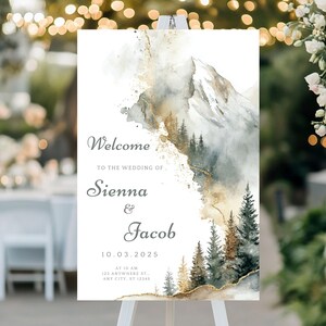Könnte beinhalten: Ein weißes Hochzeits-Willkommensschild mit Aquarell-Berg- und Waldkunst. Auf dem Schild steht "Willkommen zur Hochzeit von Sienna & Jacob 10.03.2025". Das Design umfasst goldene Akzente und eine weiche, elegante Ästhetik.