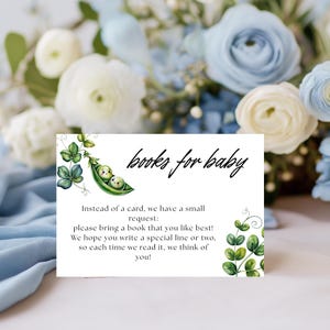 May include: A white card with the text "books for baby" in black script. The card features a watercolor illustration of two peas in a pod and green foliage. The card requests guests to bring a book.