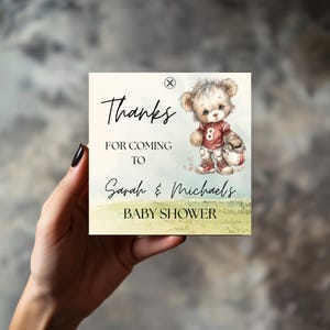 Könnte beinhalten: Quadratische Babyparty-Gefälligkeit mit Aquarelldesign. Die Karte zeigt den Text "Danke für das Kommen zur Babyparty von Sarah & Michael". Auf der rechten Seite der Karte befindet sich ein Teddybär in Football-Uniform.