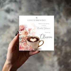 May include: White ceramic mug with a black handle, featuring the text "But First, Coffee" in black. The mug is displayed against a blurred backdrop, implying a comfortable environment.