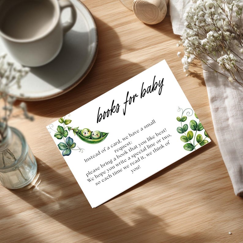 May include: White card with the text "books for baby" in cursive. The card features a watercolor illustration of two peas in a pod and green leaf accents. The card requests guests to bring a book.