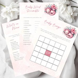 May include: Baby shower game set with a baby dragon illustration and pink flowers. Includes "Baby Word Scramble", "What's on Phone", and "Baby Bingo" games. The games are printed on white paper with a soft pink watercolour background.