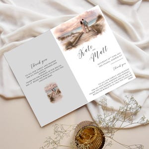 May include: A wedding invitation card, open to display the inside. The card features a watercolor illustration of a couple on a boardwalk at the beach. Text includes names, date, and a thank you message.