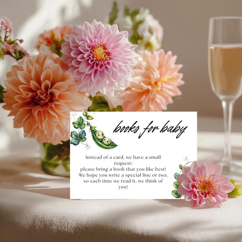 May include: A baby shower invitation card with the text "books for baby" and a watercolor illustration of two peas in a pod. The card is surrounded by peach and pink dahlias and a glass of champagne.