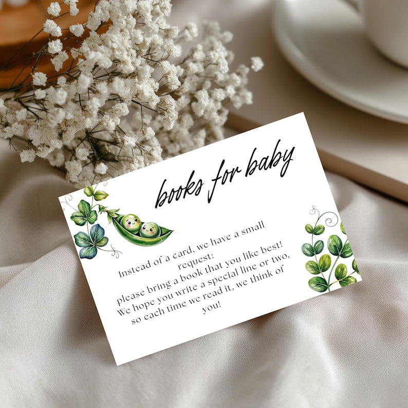 May include: A white baby shower invitation card with the text "books for baby" in black script. The card features illustrations of green leaves and two peas in a pod. The card requests guests to bring a book and write a special line.
