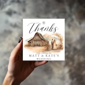 Puede incluir: Tarjeta cuadrada de agradecimiento de boda con una ilustración de acuarela de un granero, montañas y una pareja. La tarjeta dice "Gracias" en una elegante escritura, con el texto "Por venir a la boda de Matt & Kate".