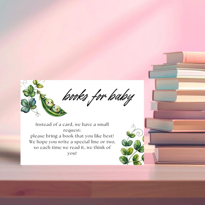 May include: A white card with the text "books for baby" and a watercolor illustration of two peas in a pod. The card requests guests to bring a book. A stack of books is visible in the background.
