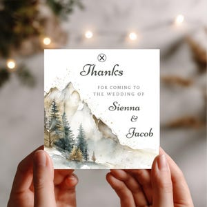 Könnte beinhalten: Quadratische Hochzeits-Dankeskarte mit Aquarell-Illustration von Bergen und Bäumen. Die Karte lautet: "Danke, dass Sie zur Hochzeit von Sienna & Jacob gekommen sind."