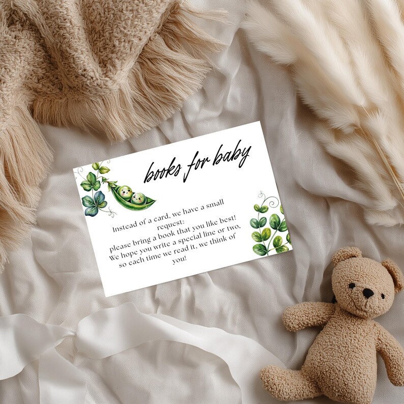 May include: A baby shower invitation card with the text "books for baby" in a script font. The card features a pea pod illustration with two baby faces and green leaf accents. A small teddy bear is in the bottom right corner.