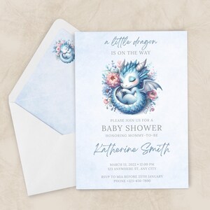 Może przedstawiać: Zaproszenie na baby shower z akwarelową ilustracją śpiącego niebieskiego smoka otoczonego kwiatami. Zaproszenie zawiera tekst "a little dragon is on the way" oraz szczegóły wydarzenia, takie jak data, godzina i miejsce.