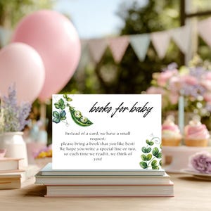May include: A white card with the text "books for baby" and a request for guests to bring a book. The card is decorated with green pea pod and leaf illustrations. Pink balloons and books are in the background, suggesting a baby shower theme.