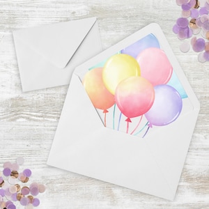 Può includere: Busta bianca con un'illustrazione ad acquerello di palloncini colorati. I palloncini sono nelle tonalità del giallo, rosa, arancione e viola. È visibile una seconda busta bianca, insieme a coriandoli sparsi.