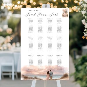 May include: A wedding seating plan displayed on a white easel. The chart lists guests' names under table numbers. The top of the chart reads "MATT & KATE" and "Find Your Seat" in cursive. A watercolour image of a couple on a beach is at the bottom.