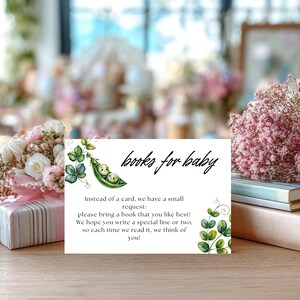 May include: A white card with the text "books for baby" and a watercolor illustration of two peas in a pod. The card requests guests to bring a book and write a special line.