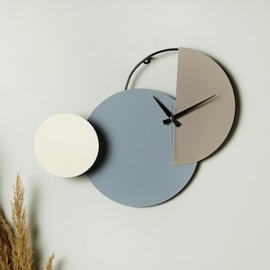 May include: A modern wall clock with a blue, beige, and white design. The clock has a black metal frame and hands.