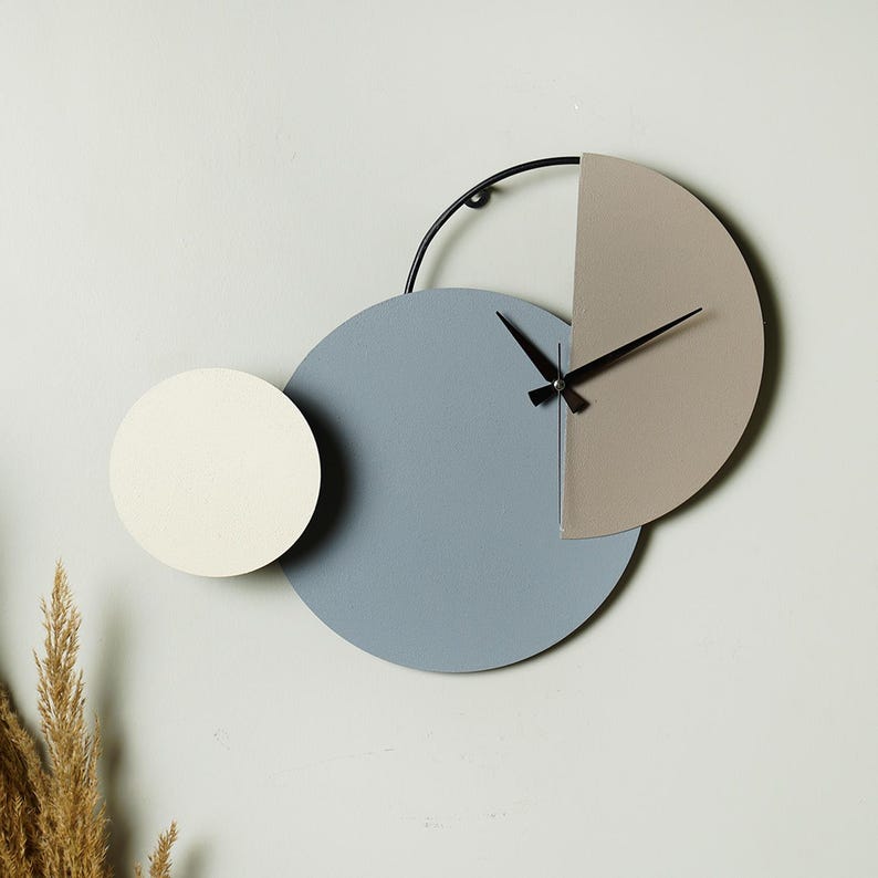 May include: A modern wall clock with a blue, beige, and white design. The clock has a black metal frame and hands.