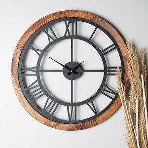 May include: A large, round, black metal clock with Roman numeral markings on a wooden frame. The clock has a black face and black hands.