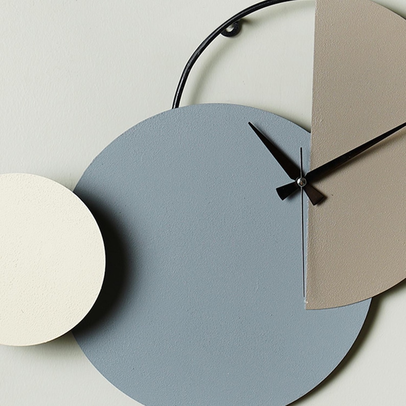May include: A modern wall clock with three overlapping circles in shades of gray, beige, and white. The clock hands are black and the clock face is minimalist.