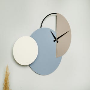 May include: A modern wall clock with three overlapping circles. The largest circle is light blue, the middle circle is white, and the smallest circle is light brown. The clock hands are black.