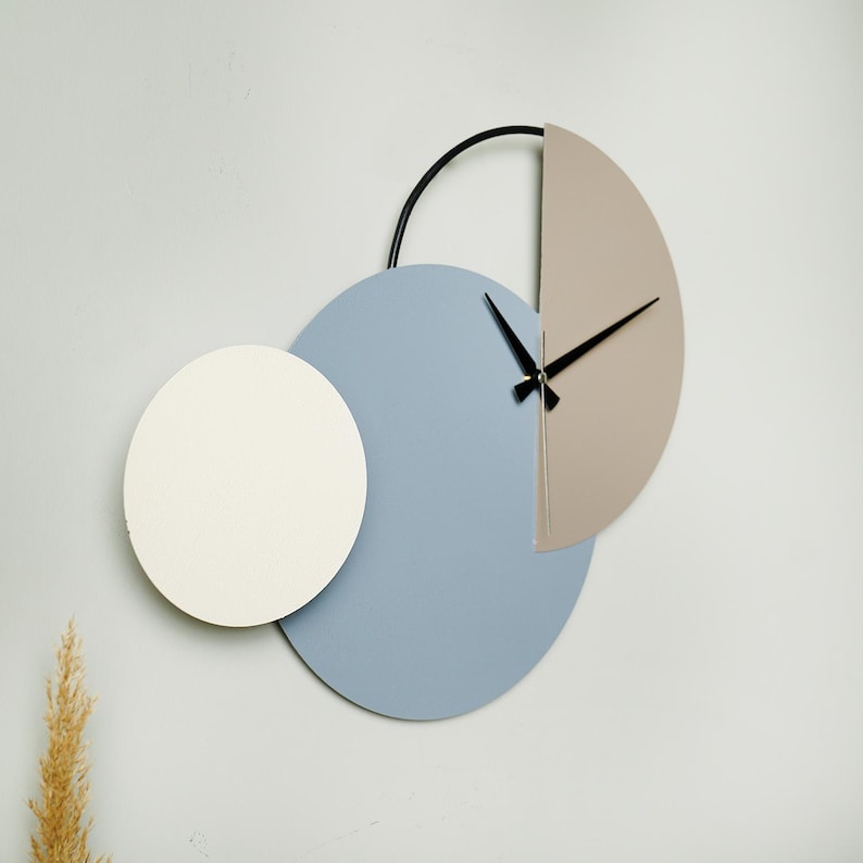 May include: A modern wall clock with three overlapping circles. The largest circle is light blue, the middle circle is white, and the smallest circle is light brown. The clock hands are black.
