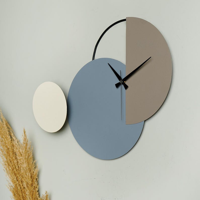 May include: A modern wall clock with three overlapping circles. The largest circle is blue, the middle circle is beige, and the smallest circle is white. The clock hands are black.
