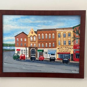 May include: A framed painting of a street scene with colorful buildings and parked cars. The painting features a blue sky with clouds and the text "Northport Sweet Shop Luncheonette". The buildings are various shades of brown, yellow, and red.