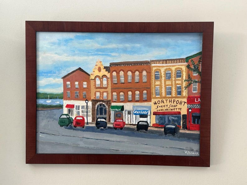 May include: A framed painting of a street scene with colorful buildings and parked cars. The painting features a blue sky with clouds and the text "Northport Sweet Shop Luncheonette". The buildings are various shades of brown, yellow, and red.