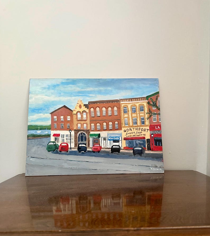 May include: An acrylic painting of a street scene with various buildings and cars. The buildings are in shades of brown, yellow, and red, with awnings and storefronts. The sky is blue with clouds. The painting is on a square canvas.