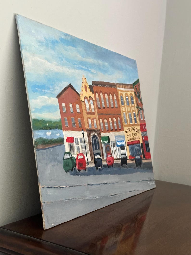 May include: An oil painting of a street scene with colorful buildings and small cars parked along the road. The sky is blue with white clouds. The painting includes the text "Northport Sweet Shop Luncheonette".