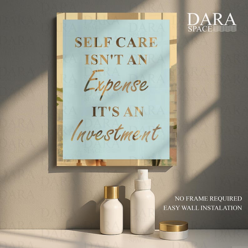 May include: A framed wall art print with the text "SELF CARE ISN'T AN EXPENSE IT'S AN INVESTMENT" in gold lettering on a light blue background. Below the print are three white cosmetic containers with gold lids.