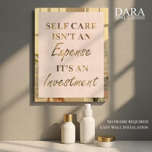 May include: A framed print with the text "SELF CARE ISN'T AN EXPENSE IT'S AN INVESTMENT" in gold lettering. Below the print are three white cosmetic containers with gold lids. The Dara Space logo is in the upper right corner.