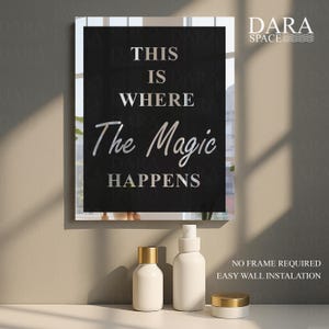 May include: A framed wall art piece with the text "THIS IS WHERE The Magic HAPPENS" in silver lettering on a black background. Below are three white cosmetic containers with gold lids.