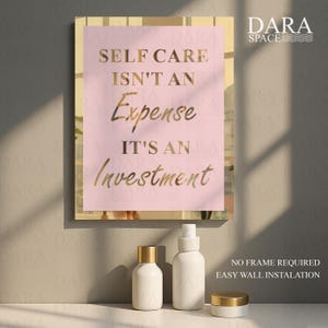 May include: A framed print with the text "SELF CARE ISN'T AN EXPENSE IT'S AN INVESTMENT" in gold lettering on a pink background. Below the print are three white cosmetic containers with gold lids. The Dara Space logo is in the upper right corner.