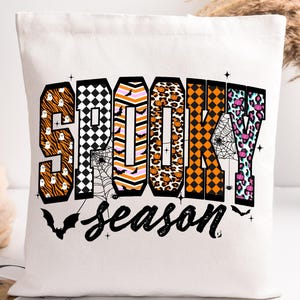 Może przedstawiać: Biała torba z napisem "SPOOKY season" w kolorowym, wzorzystym designie. Litery wypełnione są różnymi wzorami o tematyce Halloween, w tym paskami tygrysa, szachownicą i nadrukiem w cętki. Nietoperze i pajęczyny zdobią dół.