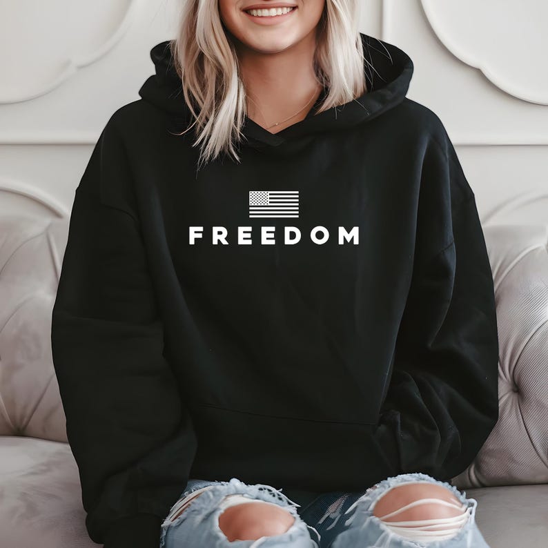 May include: Black hoodie with the word "FREEDOM" in white block letters. Above the word is a white graphic of the American flag. The hoodie has a drawstring hood and long sleeves.