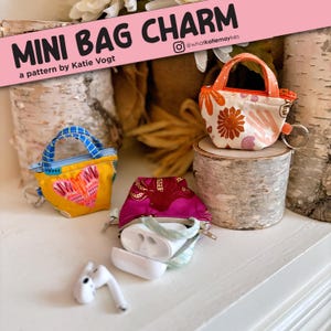 Può includere: Tre mini borse di stoffa con motivi diversi. Le borse hanno un manico superiore e una chiusura a zip. Le borse sono su una superficie di legno. Il testo "MINI BAG CHARM" è su uno sfondo rosa sopra le borse. Il testo "a pattern by Katie Vogt" è sotto le borse. Il testo "@whatkatiedidmakes" è sullo sfondo rosa.