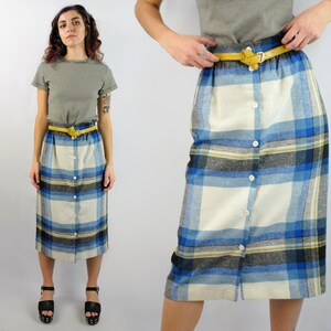 May include: A white, blue, and black plaid skirt with a button front and a yellow belt. The skirt is knee-length and has a straight silhouette.