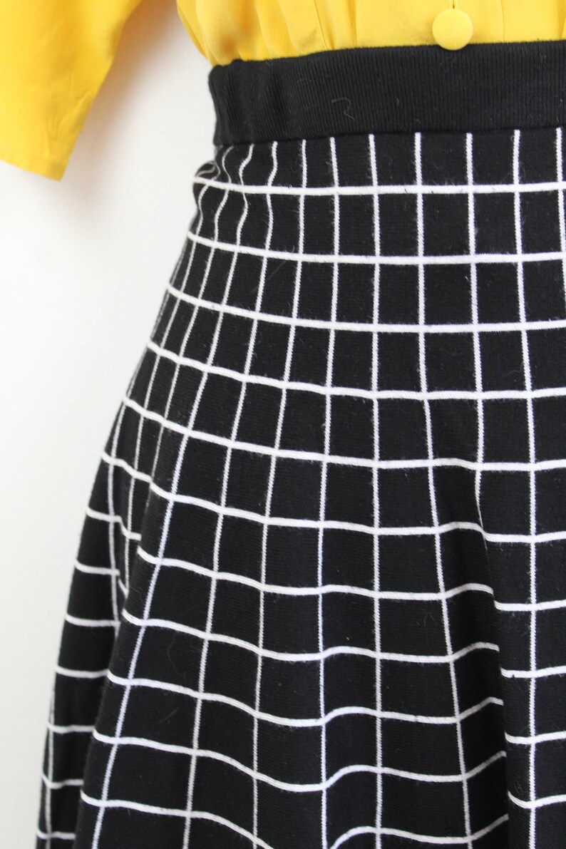 May include: Black skirt with a white grid pattern. The skirt is a-line and has a high waist.