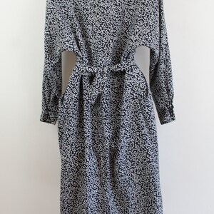 Puede incluir: Un vestido de manga larga con estampado en blanco y negro con un lazo en la cintura.