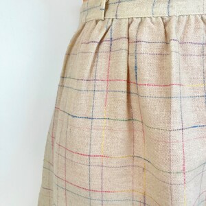 May include: A beige skirt with a multi-colored plaid pattern. The skirt has a waistband with a button closure.