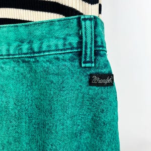 May include: Close-up of turquoise Wrangler jeans with a black and white striped top. The jeans have a textured appearance and a black Wrangler label. The top is a knit fabric with horizontal stripes.