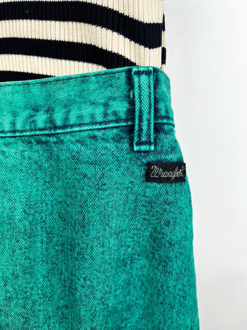 May include: Close-up of turquoise Wrangler jeans with a black and white striped top. The jeans have a textured appearance and a black Wrangler label. The top is a knit fabric with horizontal stripes.