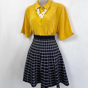 May include: A yellow short-sleeved button-down shirt with a white chain necklace and a black and white checkered skirt.