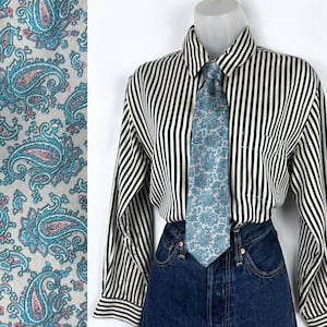 Puede incluir: Corbata azul claro con estampado de cachemir con diseños florales turquesa y rosa. Se combina con una camisa a rayas blancas y negras y vaqueros oscuros. Muestra de tela con el mismo estampado.