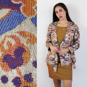 May include: A long-sleeved jacket with a colorful, geometric pattern in shades of blue, orange, and white. The jacket has a tie at the waist and is made of a woven fabric.